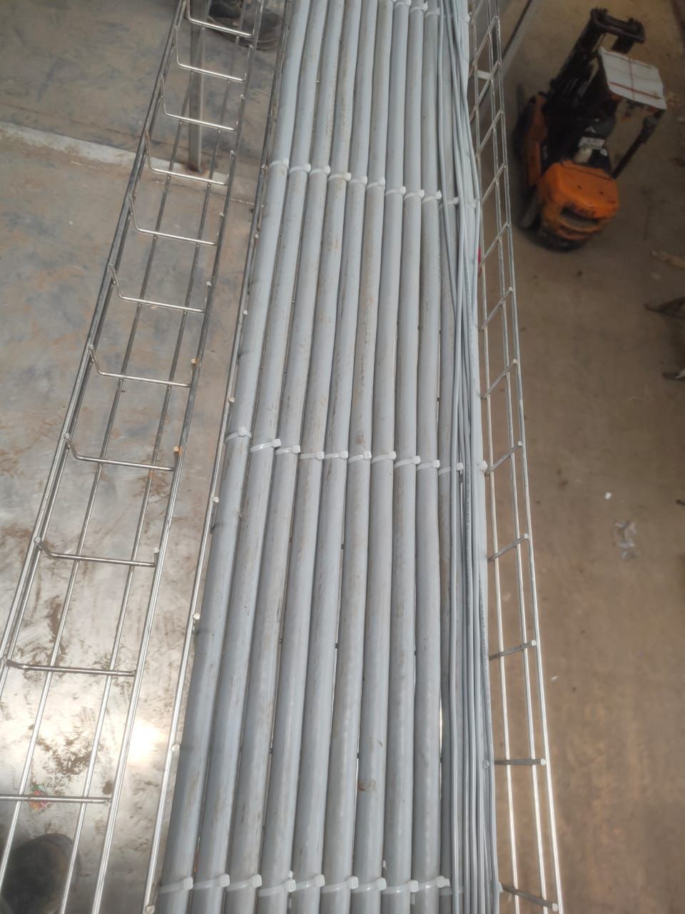 A close-up, top-down view of a wire mesh cable tray filled with neatly bundled gray cables.