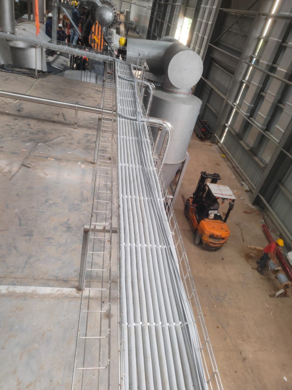 An elevated view of an industrial space with a long, filled cable tray and a forklift on the ground.