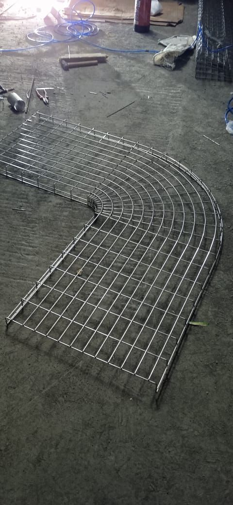 A curved section of a wire mesh cable tray lying on a concrete floor.