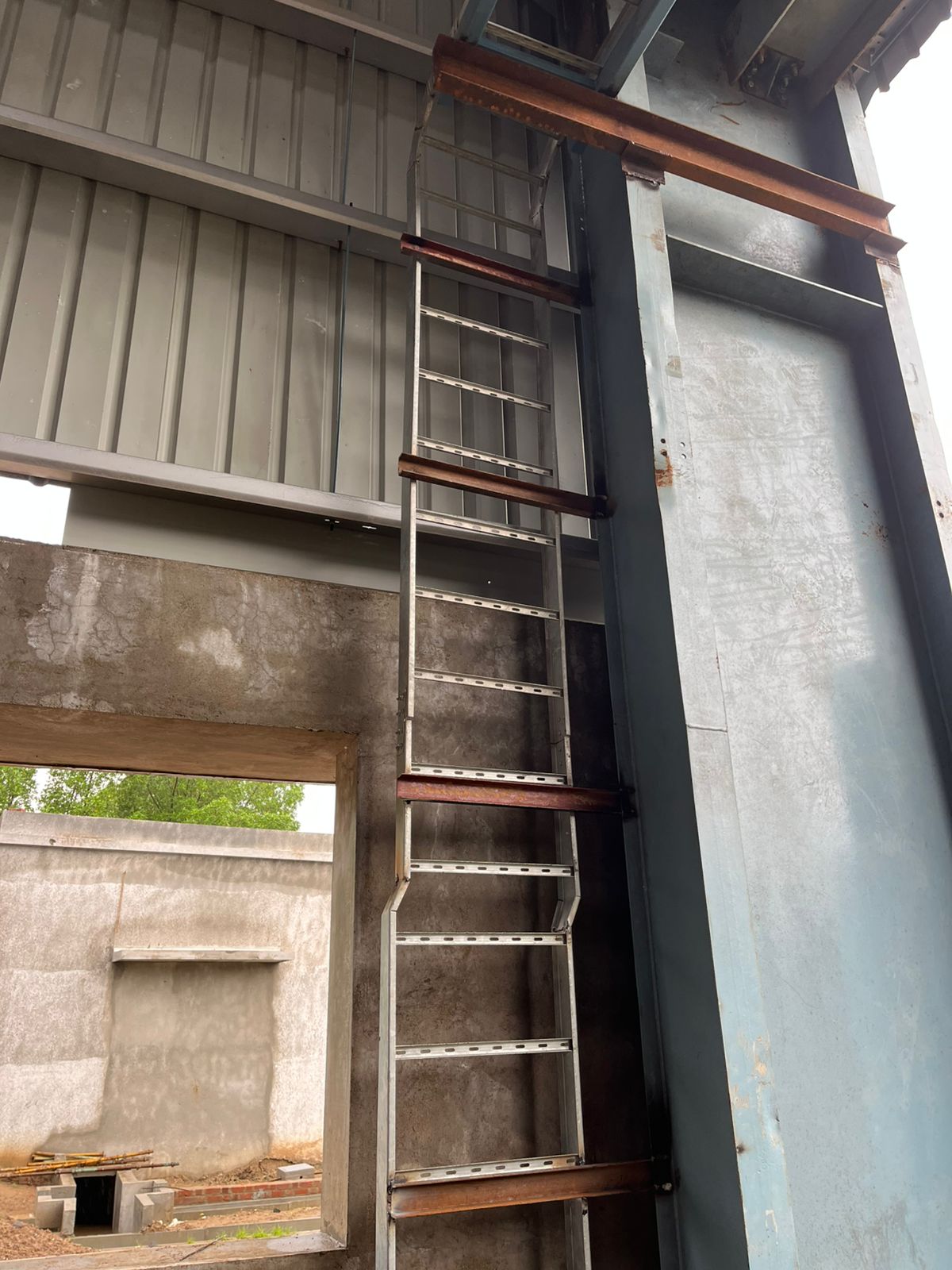 An unfinished wall with a metal ladder attached to a large steel beam.