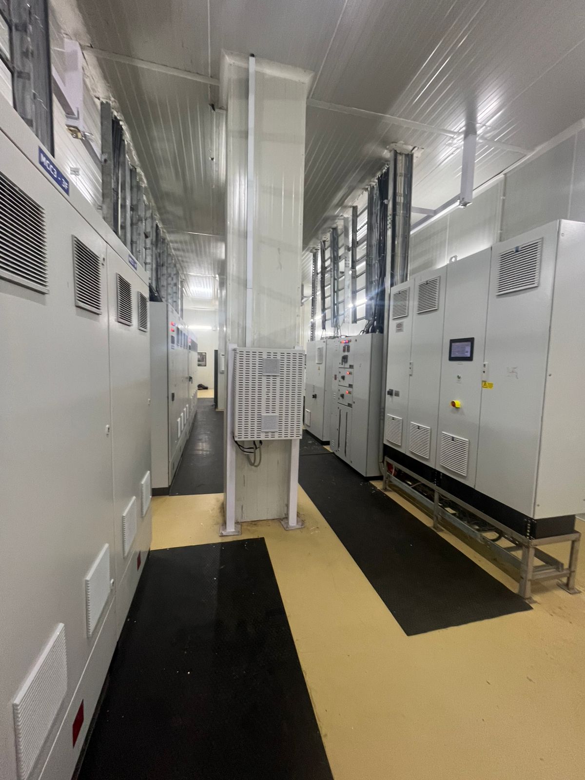 Interior view of a long hallway lined with white electrical control panels and wire racks.